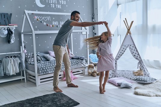 Vater und Tochter tanzen im Kinderzimmer.